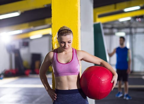 Portrait of beautiful athlete woman with red medicine  ball at crossfitness gym