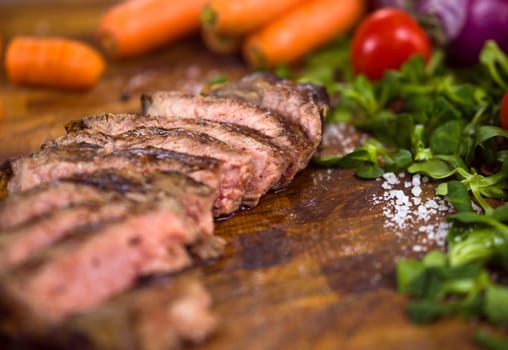 Juicy slices of grilled steak  with vegetables around on a wooden board