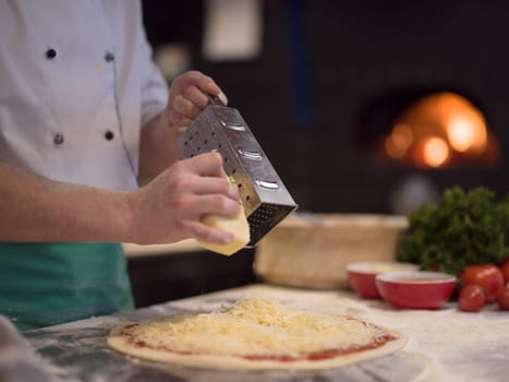 chef sprinkling cheese over fresh pizza dough on kitchen table
