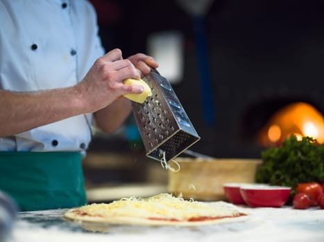 chef sprinkling cheese over fresh pizza dough on kitchen table