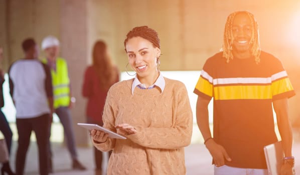 young happy multiethnic casual business couple with business team behind them using tablet computer on construction site during moving in at new startup office building