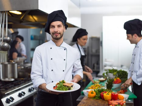 Chef holding fried Salmon fish fillet with vegetables for dinner in a restaurant kitchen