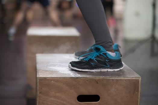 Fit young african american woman box jumping at a crossfit style gym. Female athlete is performing box jumps at gym with focus on legs