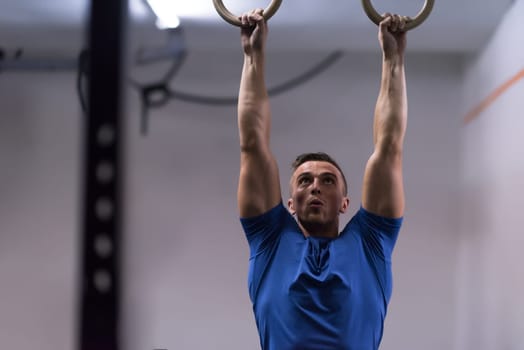Fitness handsome man doing dipping exercise using rings in the gym