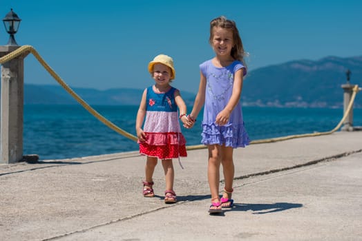 Happy smiling little sisters having fun holding their hands while walking on the beach coast during Summer vacation  Healthy childhood lifestyle concept