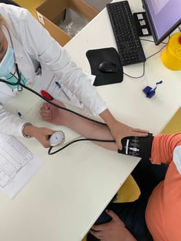 Female doctor in medical facemask measure blood pressure with electronic monitor in hospital. Caring woman GP help examine do checkup of elderly client in clinic. Healthcare, hypertension concept. High quality photo