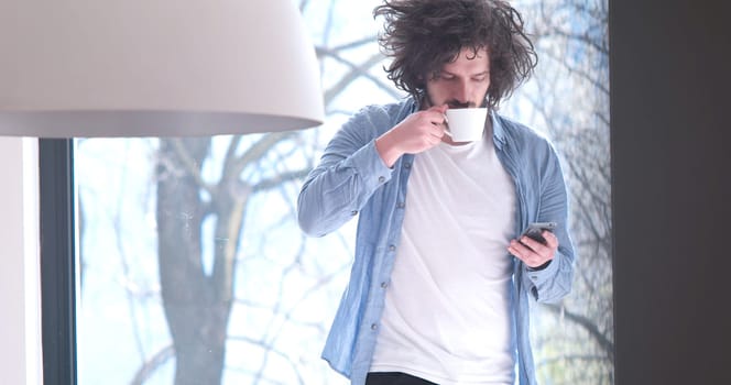 Handsome casual young man drinking coffee and using a mobile phone at  home