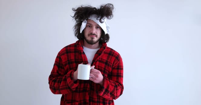 young Man with flu and fever wrapped holding cup of healing tea isolated over white