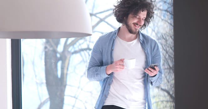 Handsome casual young man drinking coffee and using a mobile phone at  home