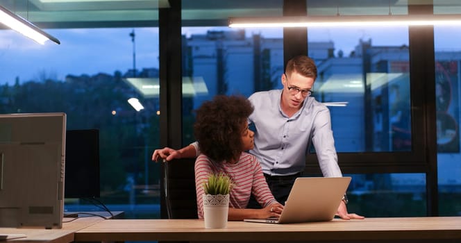 Multiethnic startup business team on meeting in modern night office interior brainstorming, working on laptop