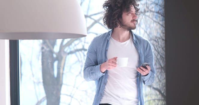 Handsome casual young man drinking coffee and using a mobile phone at  home
