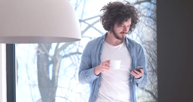 Handsome casual young man drinking coffee and using a mobile phone at  home