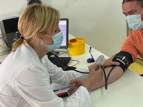 Female doctor in medical facemask measure blood pressure with electronic monitor in hospital. Caring woman GP help examine do checkup of elderly client in clinic. Healthcare, hypertension concept. High quality photo
