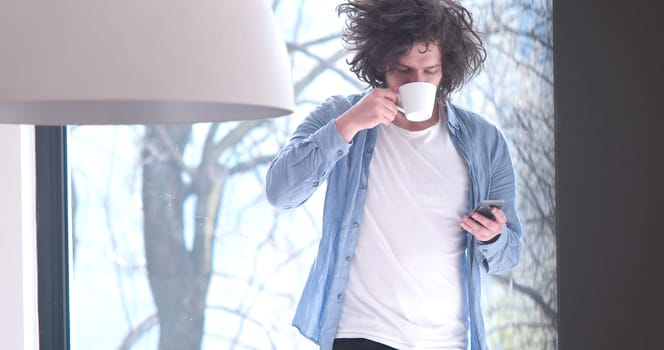 Handsome casual young man drinking coffee and using a mobile phone at  home