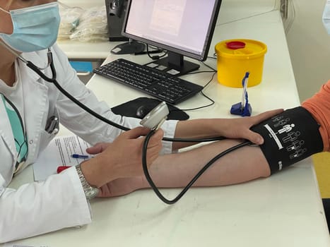 Female doctor in medical facemask measure blood pressure with electronic monitor in hospital. Caring woman GP help examine do checkup of elderly client in clinic. Healthcare, hypertension concept. High quality photo