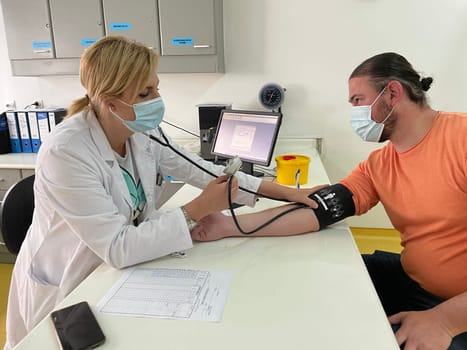 Female doctor in medical facemask measure blood pressure with electronic monitor in hospital. Caring woman GP help examine do checkup of elderly client in clinic. Healthcare, hypertension concept. High quality photo