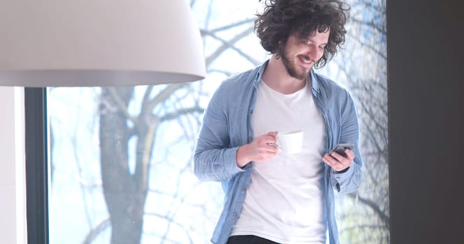 Handsome casual young man drinking coffee and using a mobile phone at  home