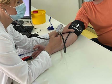 Female doctor in medical facemask measure blood pressure with electronic monitor in hospital. Caring woman GP help examine do checkup of elderly client in clinic. Healthcare, hypertension concept. High quality photo