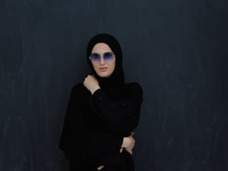 Young muslim in traditional clothes or abaya and sunglasses posing in front of black chalkboard. Arab woman representing modern arabic lifestyle, islamic fashion and Ramadan kareem concept