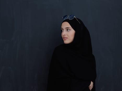 Young muslim in traditional clothes or abaya and sunglasses posing in front of black chalkboard. Arab woman representing modern arabic lifestyle, islamic fashion and Ramadan kareem concept