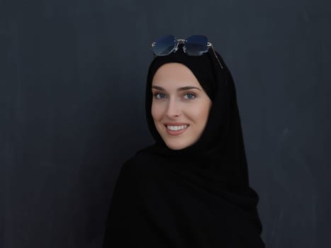 Young muslim in traditional clothes or abaya and sunglasses posing in front of black chalkboard. Arab woman representing modern arabic lifestyle, islamic fashion and Ramadan kareem concept