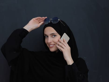 Young muslim businesswoman in traditional clothes or abaya talking on the smartphone. Arab woman in front of black chalkboard and representing techology, islamic fashion and Ramadan kareem concept
