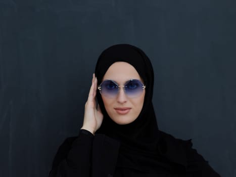 Young muslim in traditional clothes or abaya and sunglasses posing in front of black chalkboard. Arab woman representing modern arabic lifestyle, islamic fashion and Ramadan kareem concept