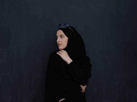 Young muslim in traditional clothes or abaya and sunglasses posing in front of black chalkboard. Arab woman representing modern arabic lifestyle, islamic fashion and Ramadan kareem concept