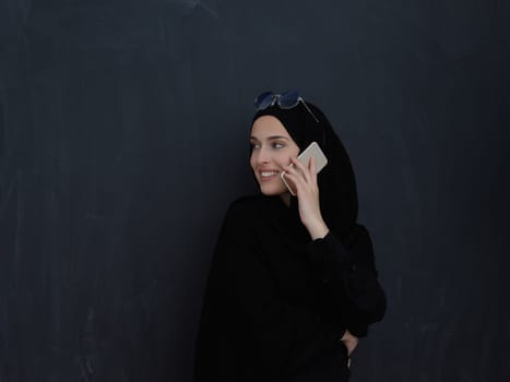 Young muslim businesswoman in traditional clothes or abaya talking on the smartphone. Arab woman in front of black chalkboard and representing techology, islamic fashion and Ramadan kareem concept