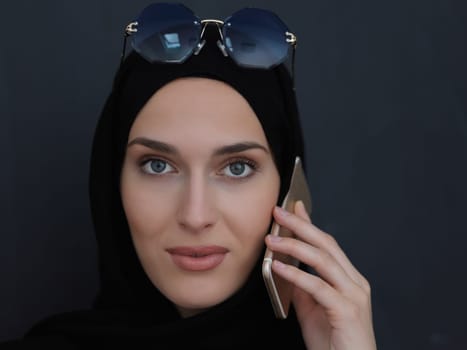 Young muslim businesswoman in traditional clothes or abaya talking on the smartphone. Arab woman in front of black chalkboard and representing techology, islamic fashion and Ramadan kareem concept