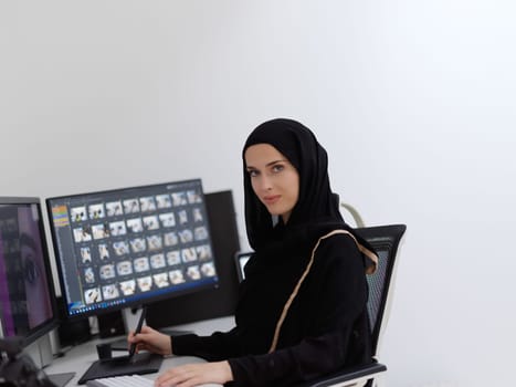 Muslim female graphic designer working on computer using graphic tablet and two monitors. Girl wearing hijab editing photos in the office