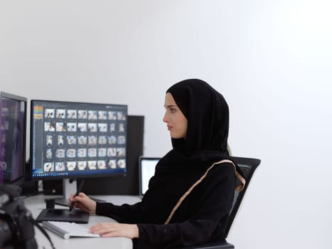 Muslim female graphic designer working on computer using graphic tablet and two monitors. Girl wearing hijab editing photos in the office
