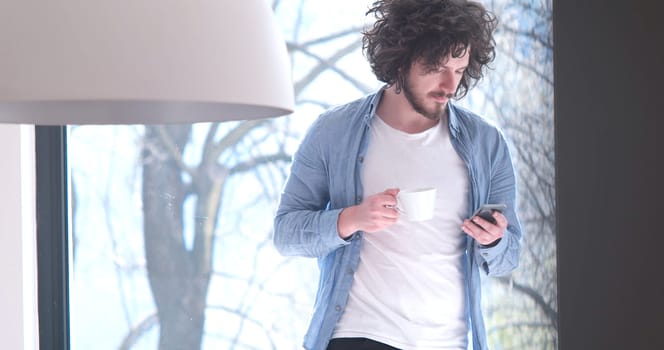 Handsome casual young man drinking coffee and using a mobile phone at  home