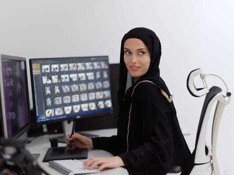 Muslim female graphic designer working on computer using graphic tablet and two monitors. Girl wearing hijab editing photos in the office
