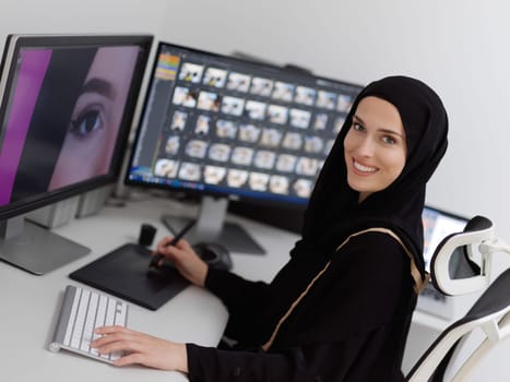 Muslim female graphic designer working on computer using graphic tablet and two monitors. Girl wearing hijab editing photos in the office