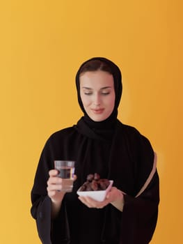 Modern muslim woman in abaya holding a date fruit and glass of water in front of her. Concept celebration of iftar time, end of fasting, in ramadan holy month
