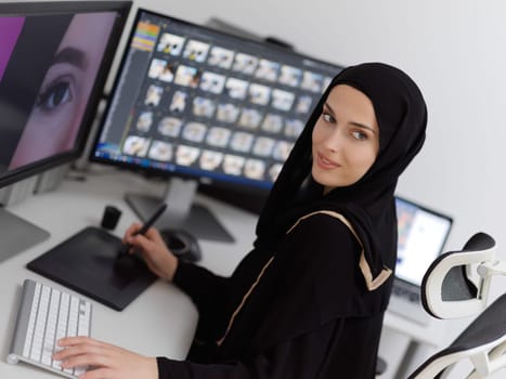 Muslim female graphic designer working on computer using graphic tablet and two monitors. Girl wearing hijab editing photos in the office