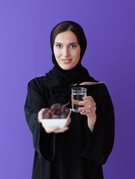 Modern muslim woman in abaya holding a date fruit and glass of water in front of her. Concept celebration of iftar time, end of fasting, in ramadan holy month