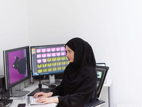 Muslim female graphic designer working on computer using graphic tablet and two monitors. Girl wearing hijab editing photos in the office