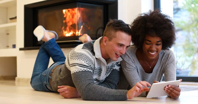 beautiful young multiethnic couple using tablet computer on the floor of their luxury home in front of fireplace at autumn day