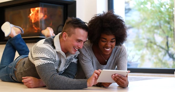beautiful young multiethnic couple using tablet computer on the floor of their luxury home in front of fireplace at autumn day