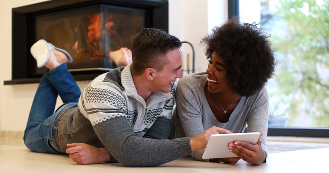 beautiful young multiethnic couple using tablet computer on the floor of their luxury home in front of fireplace at autumn day