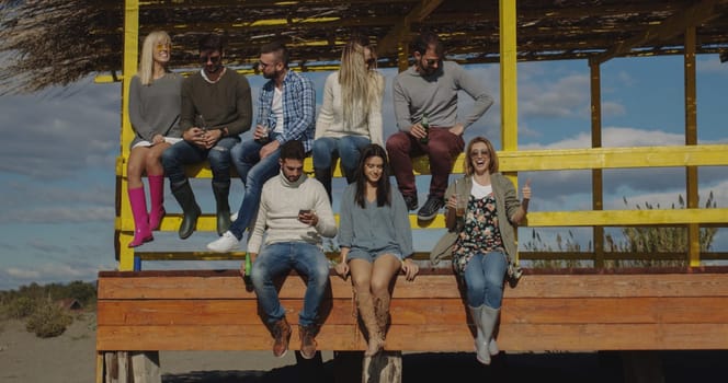 Happy Group Of Friends Hanging Out At Beach House having fun and drinking beer on autumn day