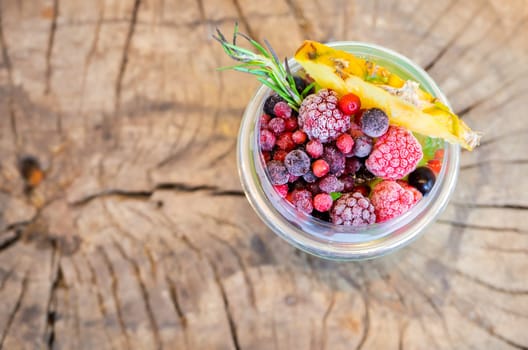 Top view of refreshing cool drink of ice tea with mixed berries (raspberry, blueberry and cranberry) and a slice of pineaple fruit in a plastic cup on wooden table
