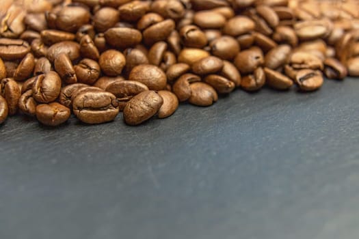 Heap of coffee beans lying on a dark slate desk forming the top edge of a photo.