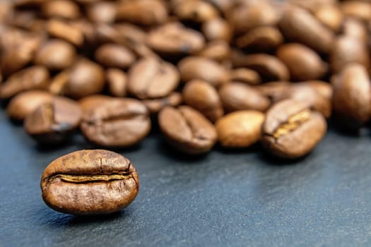 Closeup view of coffee bean lying  in front of heap of coffee beans. Horizontally.