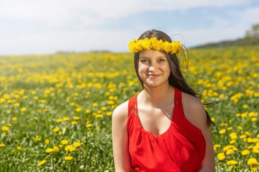 Smiling young girl posing in a dandelion meadow with a wreath of dandelions on her head.