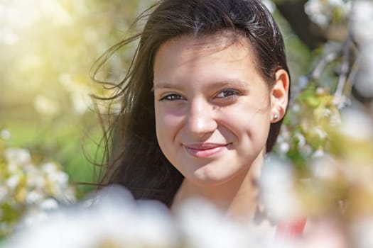 Closeup view of smiling black long hair girl posing in blooming tree.  Horizontally.