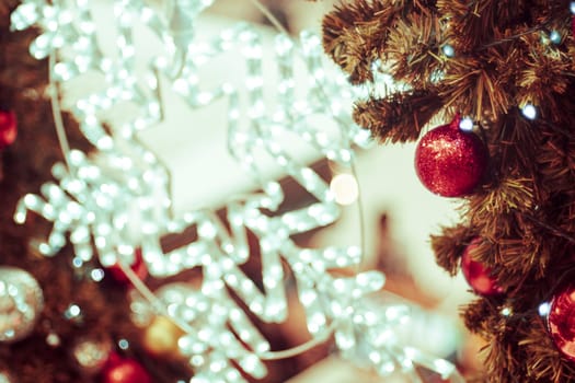 Decorated Christmas tree on blurred background. Christmas decoration. Hanging red balls on pine branches christmas tree garland and ornaments over abstract bokeh background with copy space