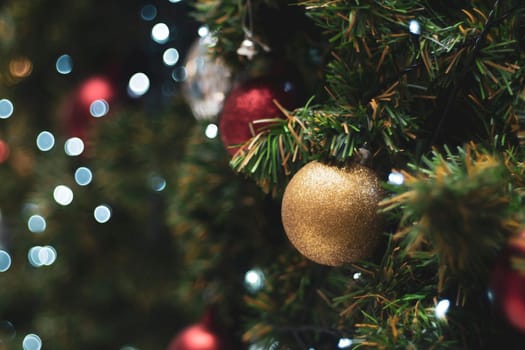 Decorated Christmas tree on blurred background. Christmas decoration. Hanging red balls on pine branches christmas tree garland and ornaments over abstract bokeh background with copy space
